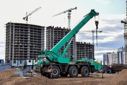 Mobile auto crane at construction site. Work of truck crane on project works. Tower cranes and builders in action. Crane for building multi-story a home