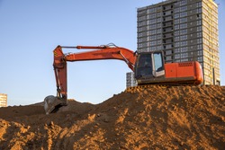 Excavator working at construction site. Backhoe during earthworks. Digging ground for the foundation and for laying sewer pipes district heating. Earth-moving heavy equipment