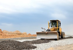 Сonstruction machine Motor Grader at a construction site level the ground and gravel stones for the construction of a new asphalt road. Road construction equipment. Roadworks concept