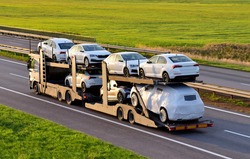 Car carrier trailer transports cars on highway on sunset background. Auto transport and car shipping services concept. Truck with Semi-remorque. Cars Shipping. Car transportation