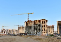 View of a large construction site with buildings under construction and multi-storey residential homes.Tower cranes in action on blue sky background. Housing renovation concept. Crane during formworks