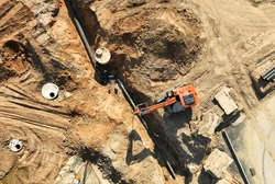 Sewage drainage system mounting at construction site. Excavator during laying sewer pipe and main systems. Civil infrastructure, water lines, sanitary sewers and storm sewers. Laying sewer pipes.