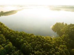 Lake in a morning mist at sunrise. River in the wild on Clear sky. Lake at dawn in fog, aerial view. Sunny morning scene in misty forest valley at river. Misty landscape. Freshwater lakes. Idyllic.