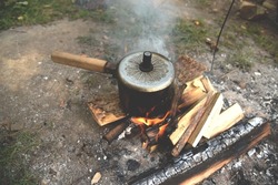 Boiling water on red hot coals in forest. Make campfire cooking. Bonfire to heat water or food while camping in nature. Camping in wildlife. Cooking on the fire. Cook Food Over a Campfire.