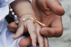 Man's hand holding the hand of a baby, on the day of his christening and with a medal of the cross.