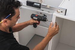 Kitchen installer using a drill to fix two pieces of a cabinet
