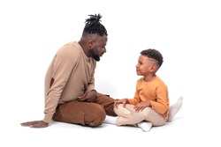 Dark skinned African male and his little son spend time together.  They sit on the floor and chat