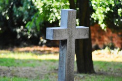 A lone standing tomb stone cross mark in a grave yard outside an old rustic church.