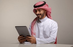 A Saudi character holding a tablet sitting in the office on a white background