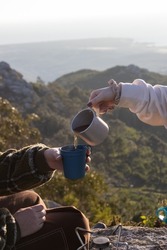 Woman pouring hot tea in cup of her girlfriend outdoors Young female backpackers drinking tea in mountains. Hiking or camping concept