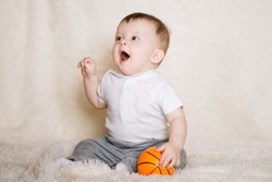 Cute young baby sitting on the floor at home and playing with a basketball, sports, healthy and active lifestyle