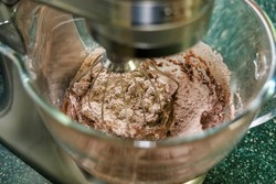 View of cake mix in a  glass bowl being mixed in a mixer.
