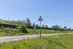 Country road with traffic signs: triangular warning caution with cyclists and maximum speed zone 60, green grass and trees in the background, sunny day with a blue sky in Netherlands