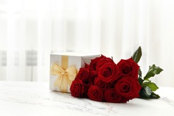 A bouquet of red roses and a gift box on the table in the interior. Love confession. Valentine's day celebration