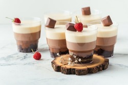 Layered dessert Trifles in a transparent glass.  Sponge biscuit and three chocolate mousse layers. Chocolate souffle trifle cake in individual disposable transparent cups. White background