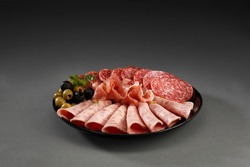 Assortment of spanish tapas or italian antipasti with , ham, salami,sausage,olives in black plate on a grey background