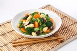 Vegan food ,Stir-Fried Vegetables ,vegetarian dish with mix of vegetables in plate on bamboo place mat on white background.