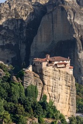 The seemingly fragile structure of Rousanou Monastery in Meteora, Greece against backdrop of a giant array of sheer cliffs and trees, vertical image