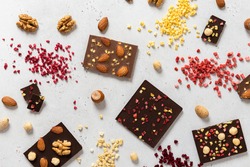 Variety of chocolate bars, nuts and ingredients on white wooden background. Handmade organic chocolate. Top view, flat lay