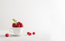 Fresh sweet raspberries in a white cup on white background. Side view, copy space for text. Natural cosmetics, food background. Summer poster, greeting card, sale