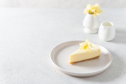 Classic New York cheesecake with fresh vanilla flower on white concrete background, side view. A piece of Vanilla cheesecake on a white plate. Confectionery menu, recipe. Copy space for text