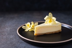 New York cheesecake or classic vanilla cheesecake with vanilla flower on a dark stone background. Side view, copy space for text. Menu, recipe, confectionery