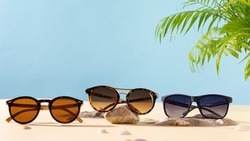 Sunglasses summer sale concept. Different sunglasses on a beach with green palm leaves. Trendy Fashion summer accessories. Copy space. Optic store. Vacation, travel concept. Sunglass offer banner