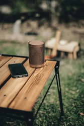 a bluetooth speaker on a wooden table with a black phone in the wild while camping