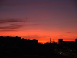 Sunset over the city. Silhouettes of buildings on the horizon against the background of the sky with clouds. Colorful orange yellow red sunset background.