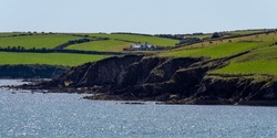 A small house on a rocky Irish shore on a sunny summer day. Atlantic coast of Ireland, landscape. Green hills. Green grass field
