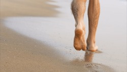 Men's feet walk along the shore line, leaving footprints