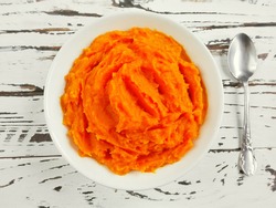 Pumpkin carrot baby puree in bowl on white wood background, top view. Fresh orange squash vegetable pumpkin carrot puree or baby mash food in bowl. Pumpkin carrot fruit smoothie of yellow food in bowl