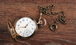 An antique gold pocket watch lies on a wooden table top view 