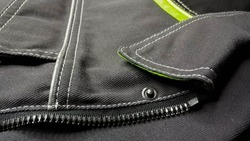 White stitching on black fabric. Texture black working clothes with white stitching closeup, green reflective elements