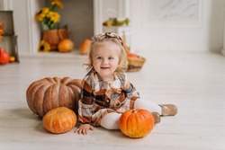 emotional portrait of a cute little happy 1 year old baby toddler kid girl in pumpkin costume is sitting on a pumpkin next to fireplace at home smiling. Halloween party concept. Easy costume idea. 