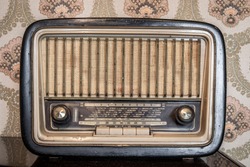 An old transistor radio, with knobs and buttons for manual tuning. In the background a vintage wallpaper. Ancient object, worn and ruined by time.