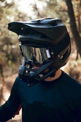 Close up of Portrait of enduro mtb or downhill mtb rider on mountain trail. Black full face helmet, goggles, blue gloves and cycling gear in the forest in winter.