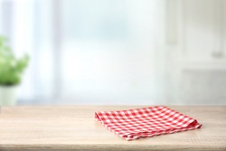 Red checkered folded picnic cloth on wooden table empty space background.Towel over the plank blurred kitchen background.