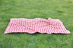 Red picnic blanket on green grass background,empty space gingham tablecloth outdoors food advertisement design.Easter decorative backdrop.