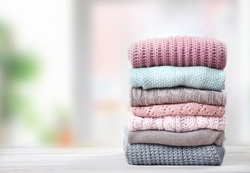 Stack of knitted textured clothing on table empty space.Colorful winter clothes,warm apparel.Heap of knitwear.Autumn garment.