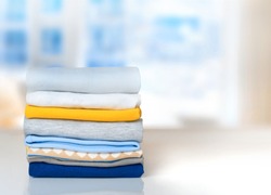 Cotton stack of colorful folded clothes on white table indoors empty space background.Household concept.Clean laundry pile.