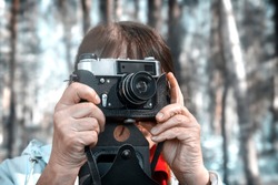 In the forest among the trees, a woman looks at the camera viewfinder, taking pictures of nature.