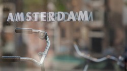Soft selective focus of AMSTERDAM letters by outdoor bike shop window, Blurred reflection on the mirror with the bicycle handlebar from another side of street parked, Netherlands land of bicycles.