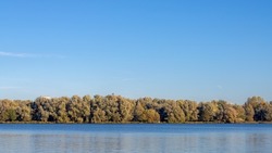 Landscape view from Nieuwe Meer (new lake) with colourful leaves on the tree in Autumn, Oeverlanden park with trees along the water under blue clear sky, Amsterdam, Netherlands.