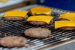 Selective focus of grilled beef burger on the charcoal stove with fire, Hamburger with golden cheese on top, Outdoor party food with barbeque (BBQ)