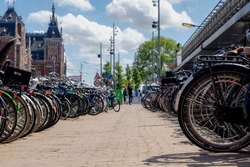 Selective focus of back wheel of bicycle under blue sky, Outdoor public parking area with blurred view of Amsterdam central station building, Cycling is a common mode of transport in the Netherlands.