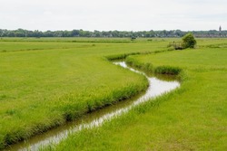 Summer countryside landscape with flat and low land, Typical Dutch polder with green meadow and the fence, Small canal or ditch with wooden bridge between the grass field, Noord Holland, Netherlands.