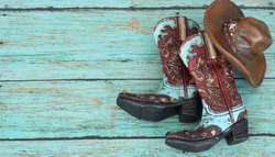teal and burnt red cowboy boots and hat on a teal wooden background with writing space
