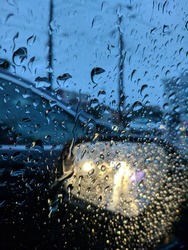 Raindrops on car window and rear view mirror. Abstract traffic in rainy day. Blurred vehicle driving in the heavy rain and slippery road. Driving in the rain