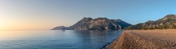 Panoramic landscape of coast of the Mediterranean sea bay at the sunrise, early morning sea scene. Fishing boat on the background of Mount Musa-Dag at dawn, the village of Cirali, Turkey.